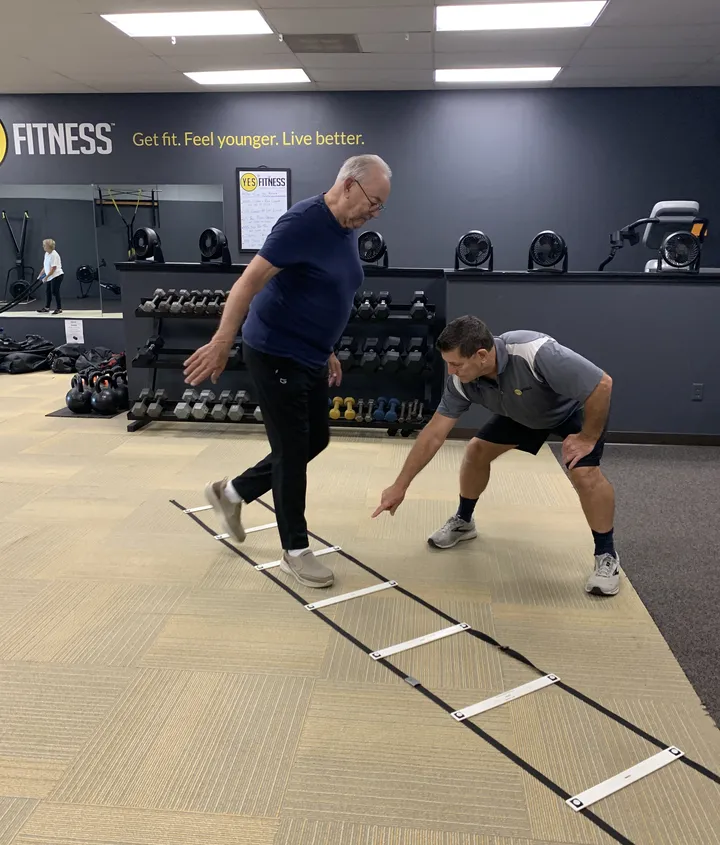 John stepping through an agility ladder drill while his coach guides his footwork at YES Fitness